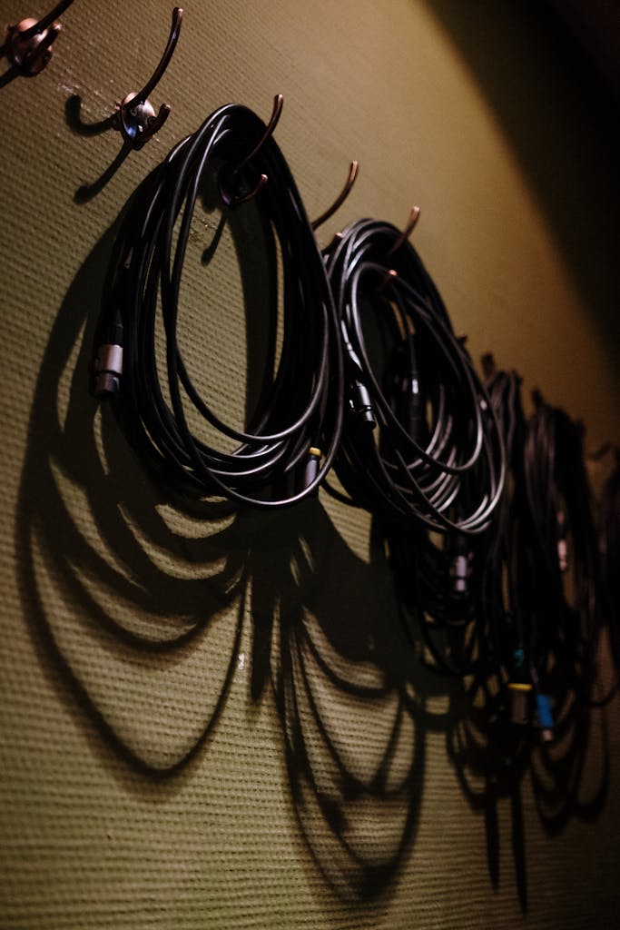 Coiled black cables hanging on hooks casting shadows on a textured wall.