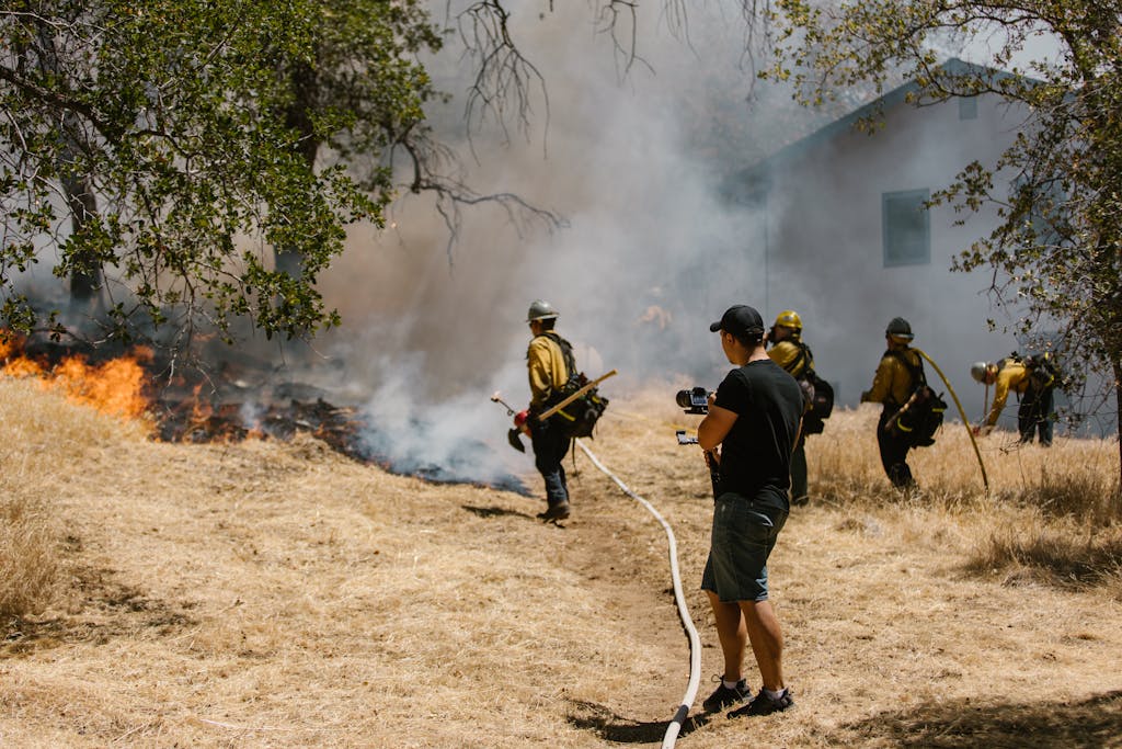 Firefighters in protective gear combating a spreading wildfire near a home.